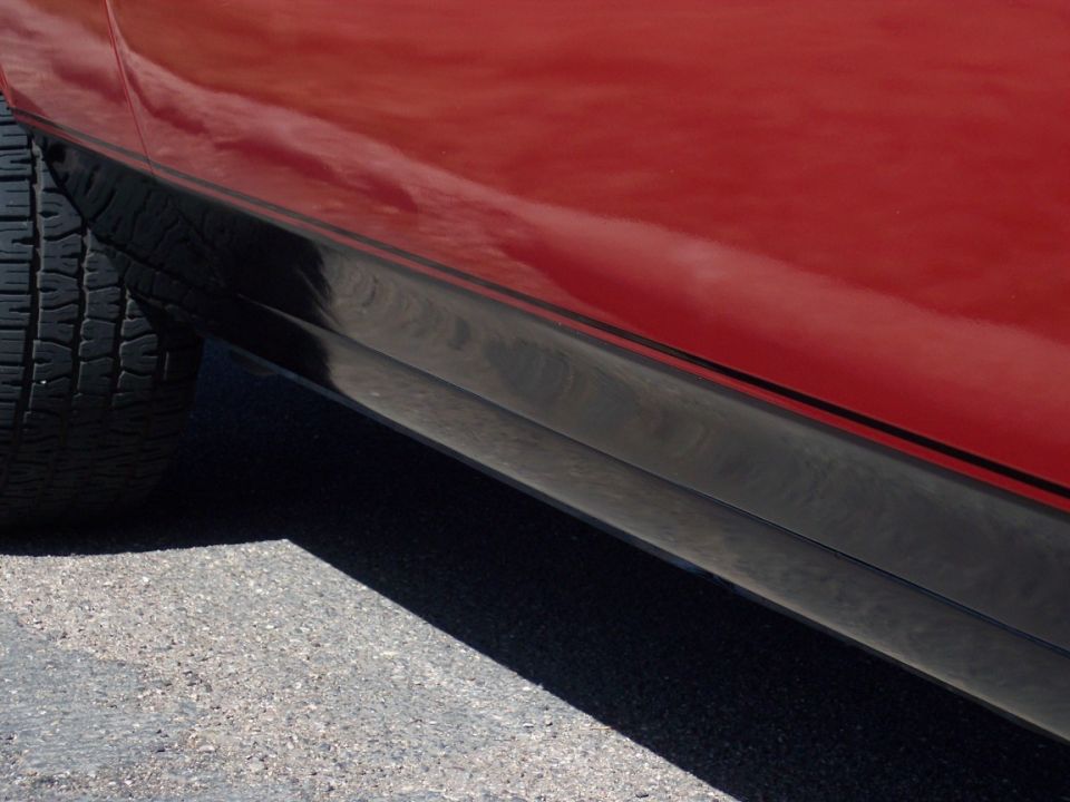 Close-up of a red car's lower body and black rocker molding behind the front tire