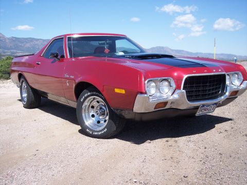 1972 Ford Ranchero - This red 1972 Ford Ranchero features a black hood stripe and chrome wheels, seen here on a dusty lot with mountains in the background.