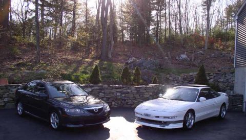 1996 Ford Probe - Two cars are parked in front of a house with trees in the background. The white car is a coupe and the black car is a sedan.