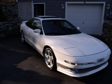 1996 Ford Probe - A white 1996 Ford Probe GT is parked in front of a garage, with sunlight casting shadows on the driveway.