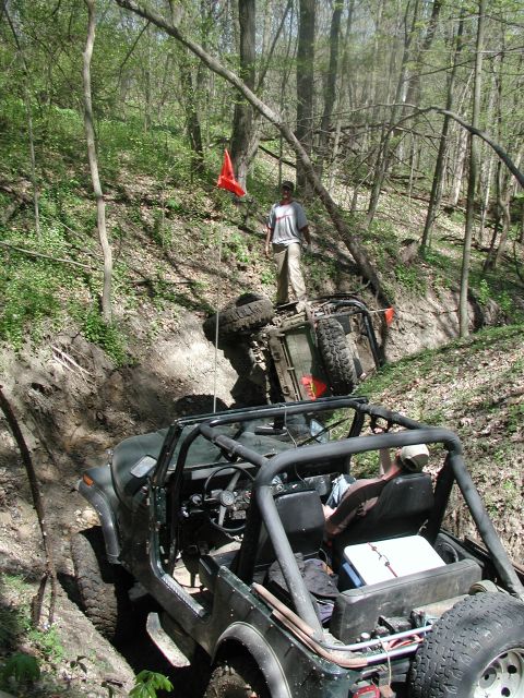 1992 Ford Bronco - Two off-road vehicles are stuck in a wooded area, with one overturned in a ditch.
