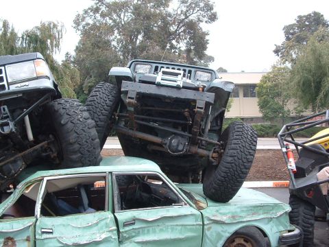 1994 Jeep YJ - A green 1994 Jeep YJ is precariously balanced on top of a severely damaged sedan, with another vehicle visible to the left.