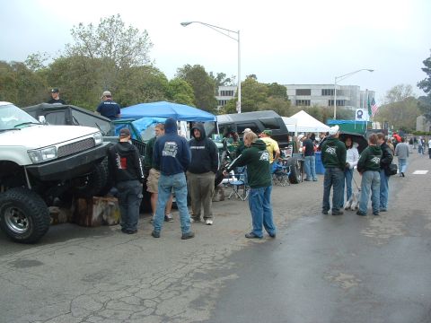 1994 Jeep YJ - Modified off-road vehicles and people gather at an outdoor event, with tents and buildings in the background.