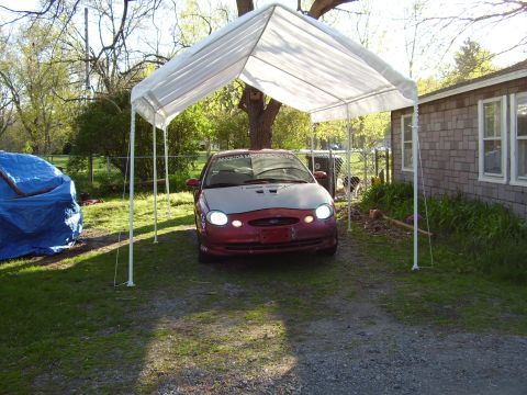 1997 Ford Taurus - A red and silver Ford Taurus is parked under a white canopy in a driveway, with a house and trees in the background.