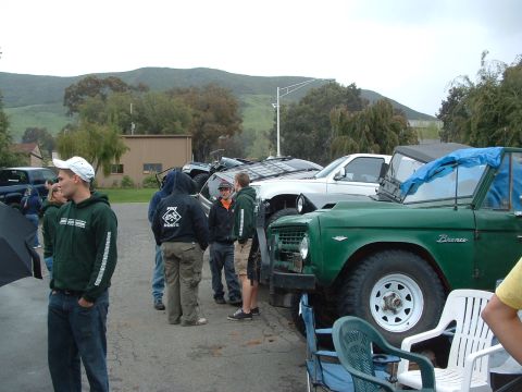 1994 Jeep YJ - A green Bronco is parked outdoors, partially covered with a blue tarp, with several people standing around it.