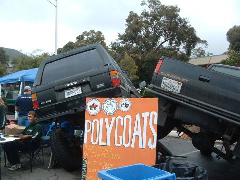 1994 Jeep YJ - A black Toyota 4Runner is dramatically lifted onto the back of a Chevrolet truck, displayed next to a large 'POLYCOATS' sign.