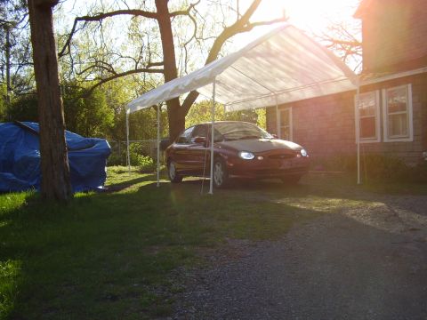 1997 Ford Taurus - A 1997 Ford Taurus sits under a temporary carport on a sunny day, with a tarp-covered object nearby.