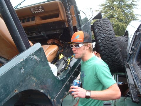 1994 Jeep YJ - Man drinks from a can inside a green Jeep YJ, with a spare tire mounted on the back.