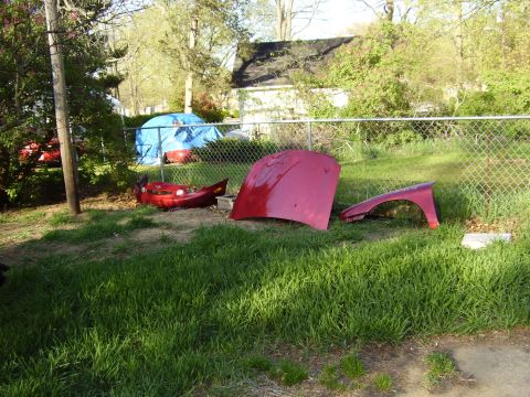 1997 Ford Taurus - Several red car body panels are visible in a grassy yard next to a chain-link fence.