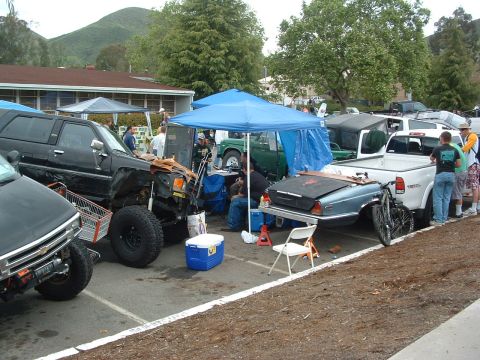 1994 Jeep YJ - An outdoor gathering features several vehicles, including a modified SUV and a car being transported on a trailer.