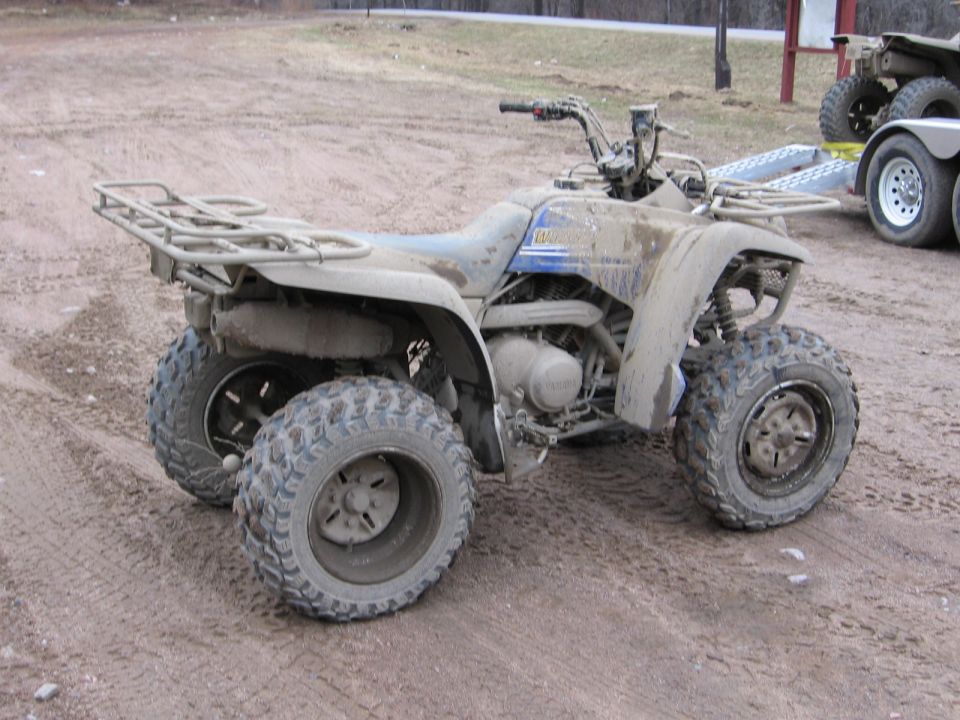 Mud-covered blue Yamaha ATV with rear rack parked on a dirt lot
