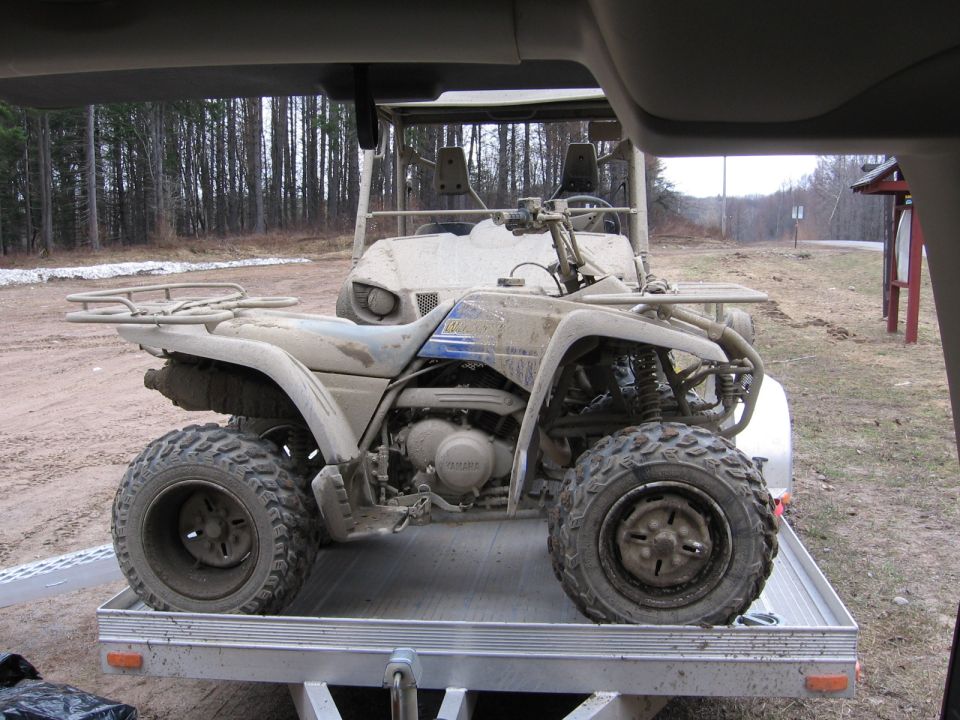 Muddy Yamaha ATV loaded sideways on an aluminum trailer outdoors