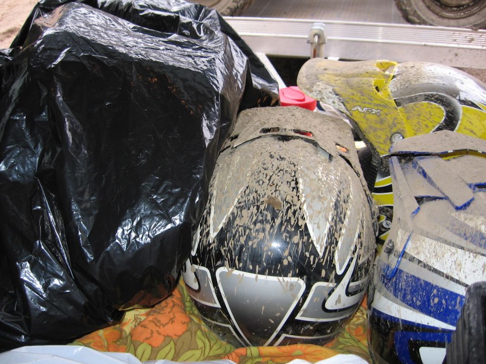 Two muddy motocross helmets, black/silver and yellow/blue, in a truck bed