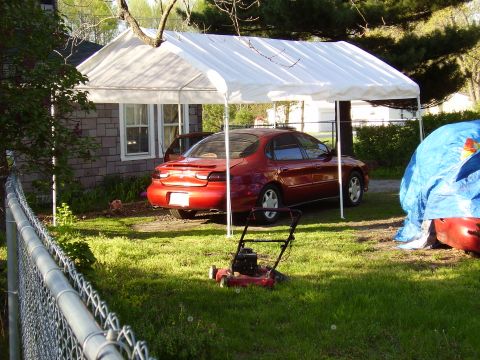 1997 Ford Taurus - A red sedan is parked under a white canopy in a grassy yard next to a house.