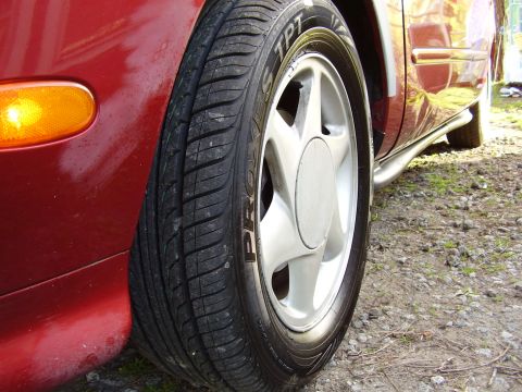 1997 Ford Taurus - A close-up view of a red vehicle's wheel and fender, showing the tire and a portion of the body.