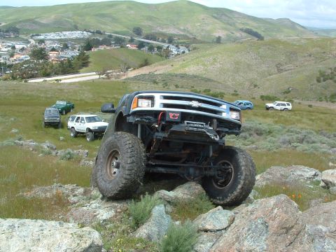 1994 Jeep YJ - Modified Chevrolet pickup truck navigating rocky terrain with other vehicles in the distance.