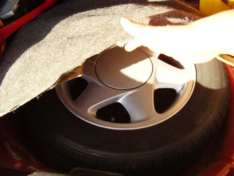1997 Ford Taurus - A hand lifts the carpet to reveal the spare tire and wheel in the trunk of a vehicle.