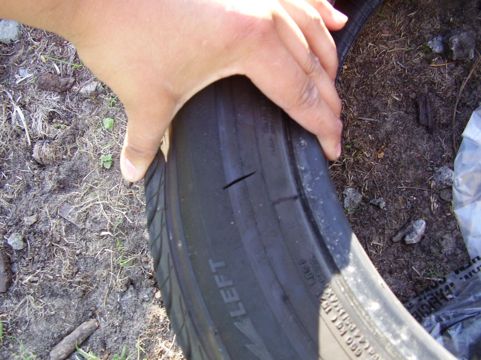 Close-up of a tire with two cuts in the tread. A hand is pressing on the sidewall