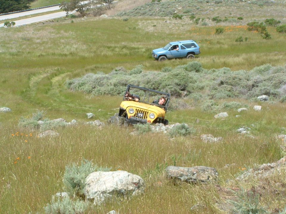 Yellow Jeep CJ-7 and blue SUV driving off-road on a grassy hill