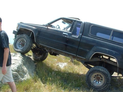 1994 Jeep YJ - A black pickup truck with a camper shell navigates a rocky incline off-road.