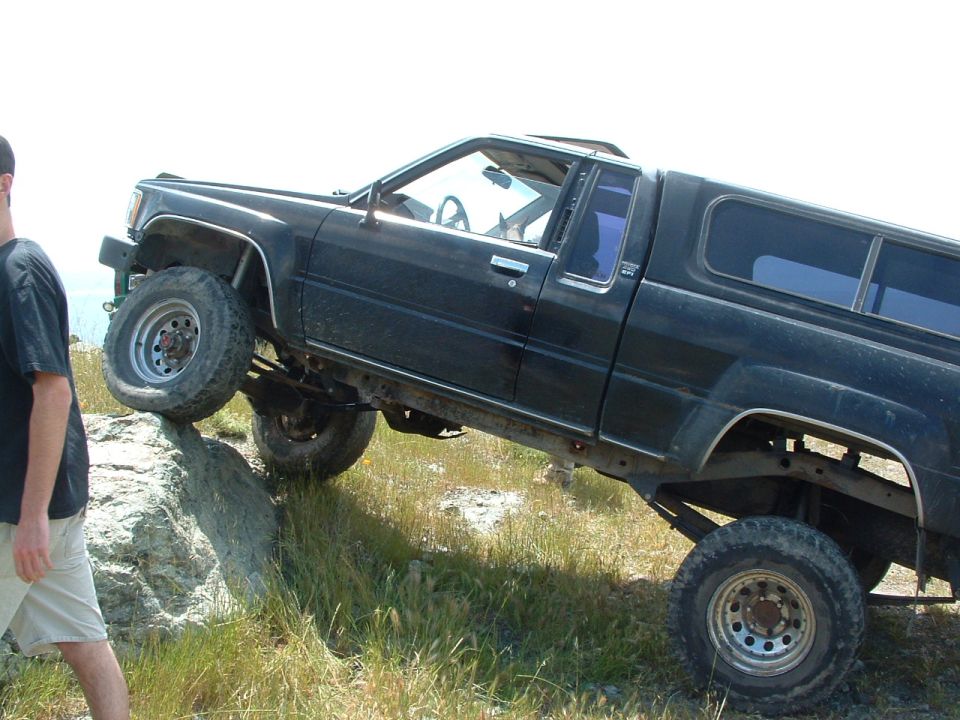 Black pickup truck with camper shell climbing a rock