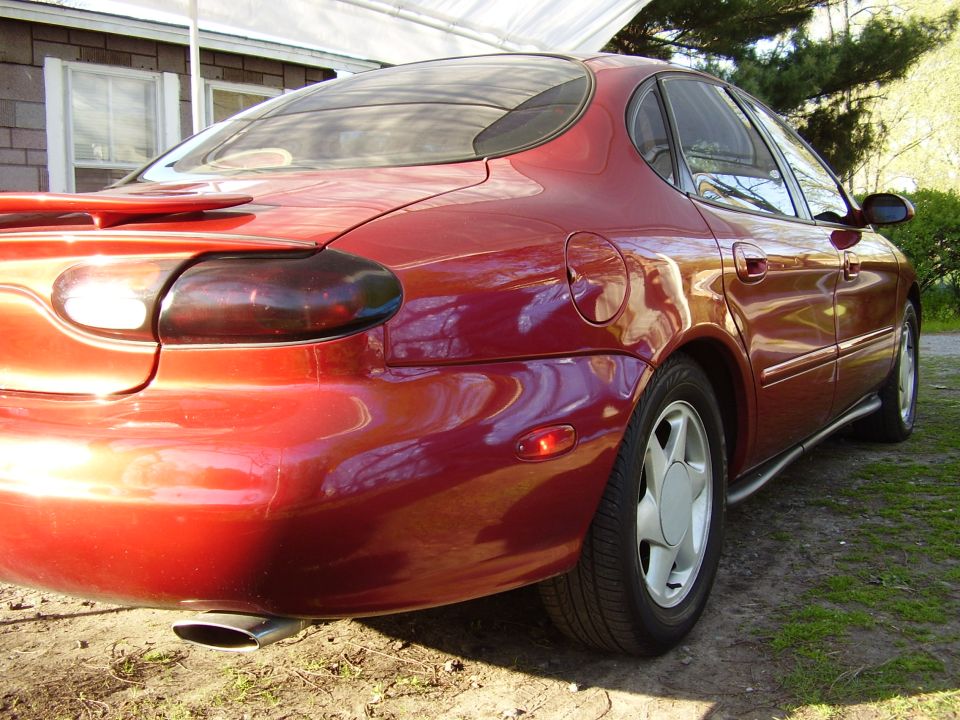Red sedan parked outside a house, showing the rear quarter panel and taillight