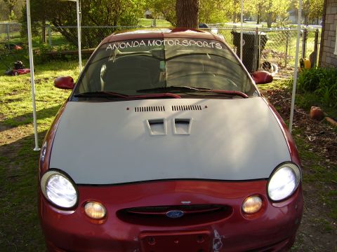 1997 Ford Taurus - The front of a red 1997 Ford Taurus is shown, a custom gray hood with air vents and a windshield banner.