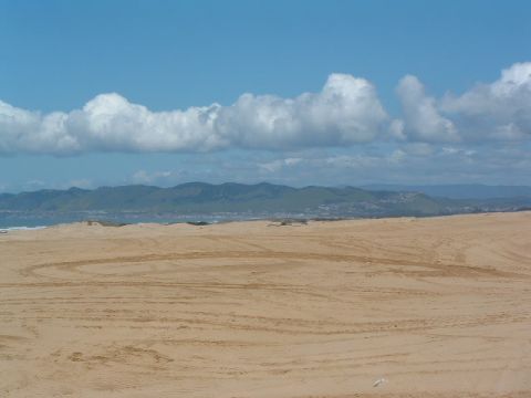1994 Jeep YJ - Tire tracks mark the sand dunes under a partly cloudy sky with distant mountains.