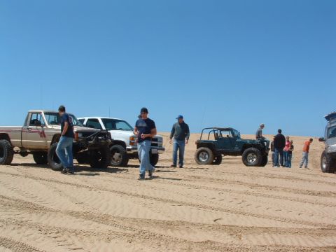 1994 Jeep YJ - A group of people and their off-road vehicles are parked on sandy terrain with tire tracks visible.