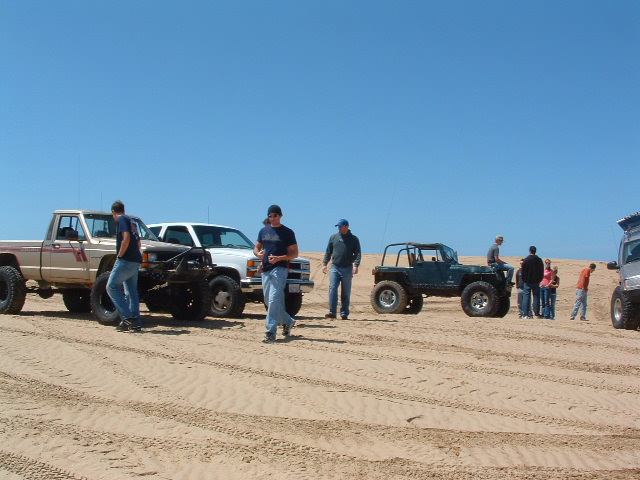 Several off-road vehicles and people gathered on sand dunes under a clear blue sky
