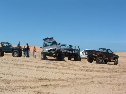 1994 Jeep YJ - Several off-road vehicles are parked on sand dunes under a clear blue sky.