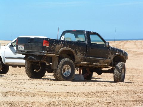 1994 Jeep YJ - A black pickup truck with a lifted suspension is being worked on while parked on a sandy beach next to a white vehicle.