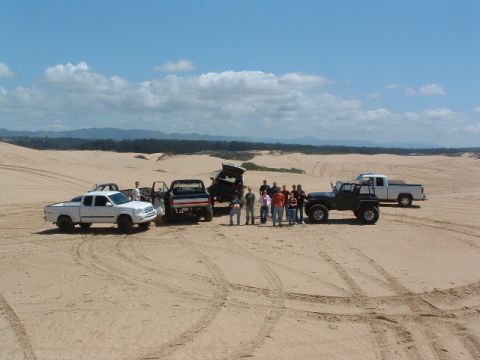 1994 Jeep YJ - Several off-road vehicles and a group of people gathered on sand dunes under a partly cloudy sky.