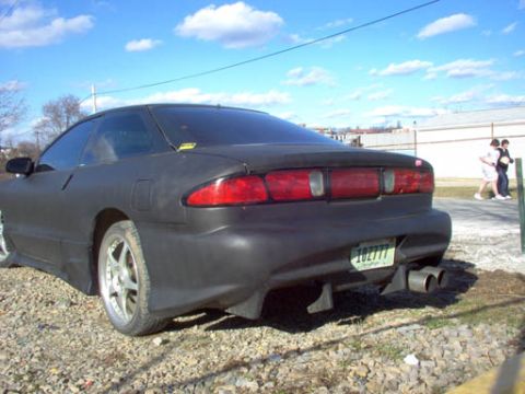 1994 Ford Probe - A matte black coupe with a distinctive rear bumper and dual exhaust pipes is parked on a gravel lot.