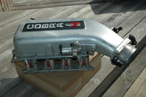 2000 Ford Mustang - A Cobra intake manifold sits on a wooden deck, showing the fuel injectors and branding.