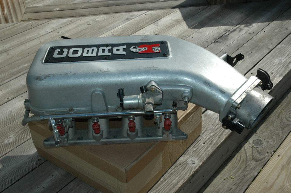 Silver Cobra intake manifold with red fuel injectors and throttle elbow on a wooden deck