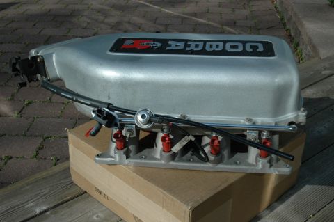 2000 Ford Mustang - A silver Cobra intake manifold with visible fuel injectors and hoses is shown against a backdrop of wooden planks and paving stones.