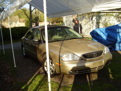 1997 Ford Taurus - Gold sedan parked under a tent with a blue tarp covering something to the right.