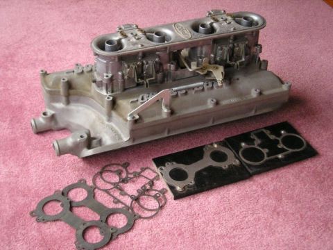 2000 Ford Mustang - A Ford intake manifold with carburetors and gaskets is displayed on a pink textured surface.