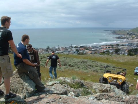 1994 Jeep YJ - A yellow Jeep CJ-7 navigates a rocky hillside overlooking a coastal town and the ocean.