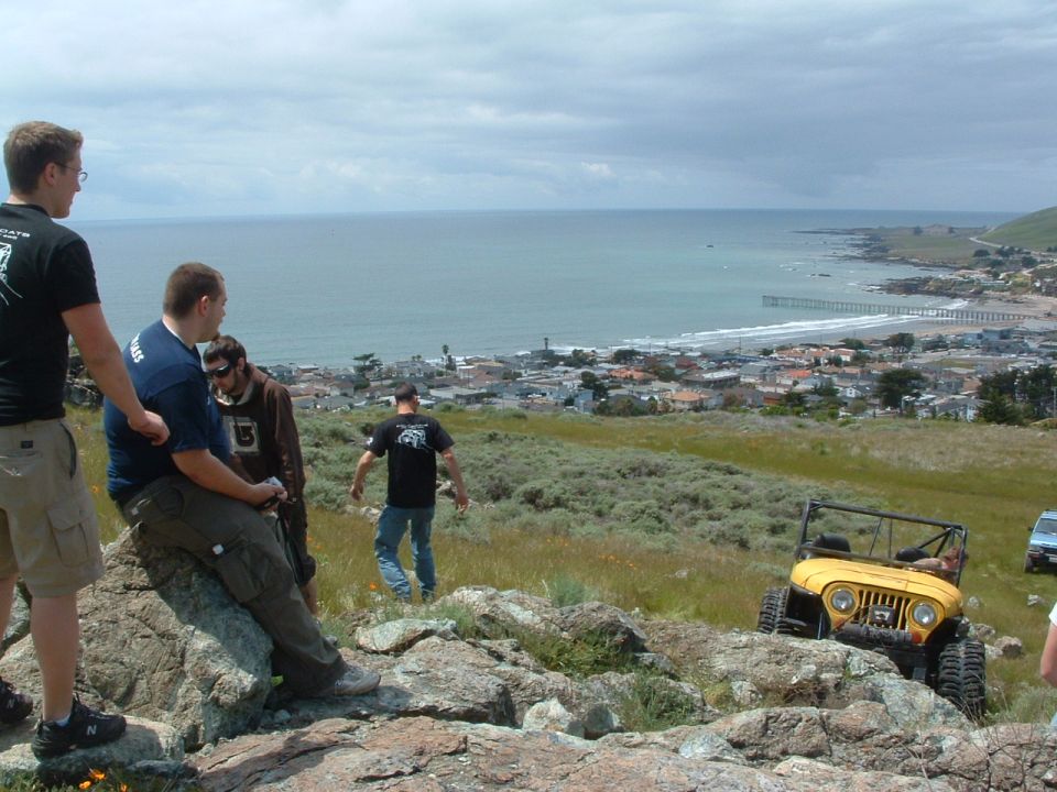 Yellow Jeep CJ-7 on rocky terrain with coastal town in background