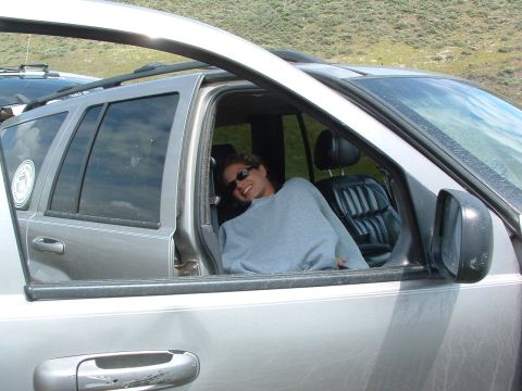 1994 Jeep YJ - A woman smiles from inside a silver SUV parked outdoors with a hilly background.