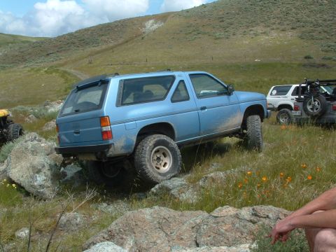 1994 Jeep YJ - A blue SUV navigates a rocky trail with other vehicles in the distance.