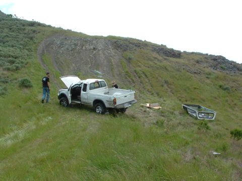 1994 Jeep YJ - A white pickup truck sits on a grassy slope with its hood and driver's door open, while its truck cap rests on the ground nearby.