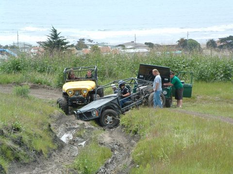 1994 Jeep YJ - Several off-road vehicles navigate a challenging muddy terrain with the ocean visible in the background.