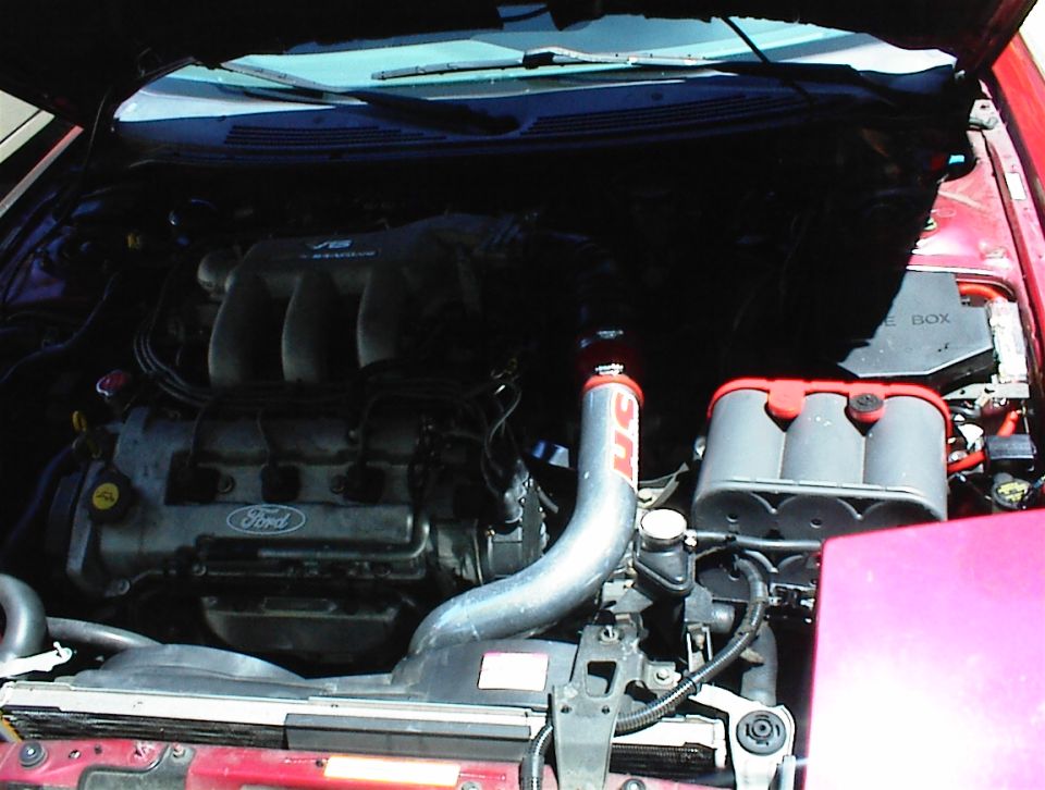 Ford V6 engine bay with cold air intake tube and red strut tower, front-clip removed