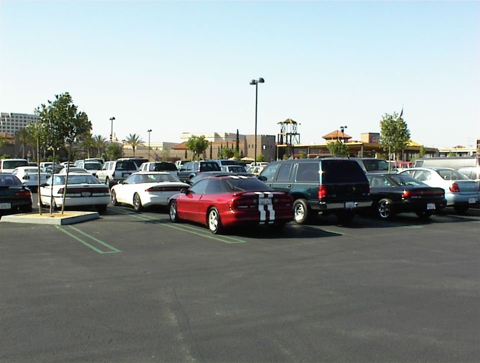 Red Ford Probe with white racing stripes parked in a lot, rear view among other cars