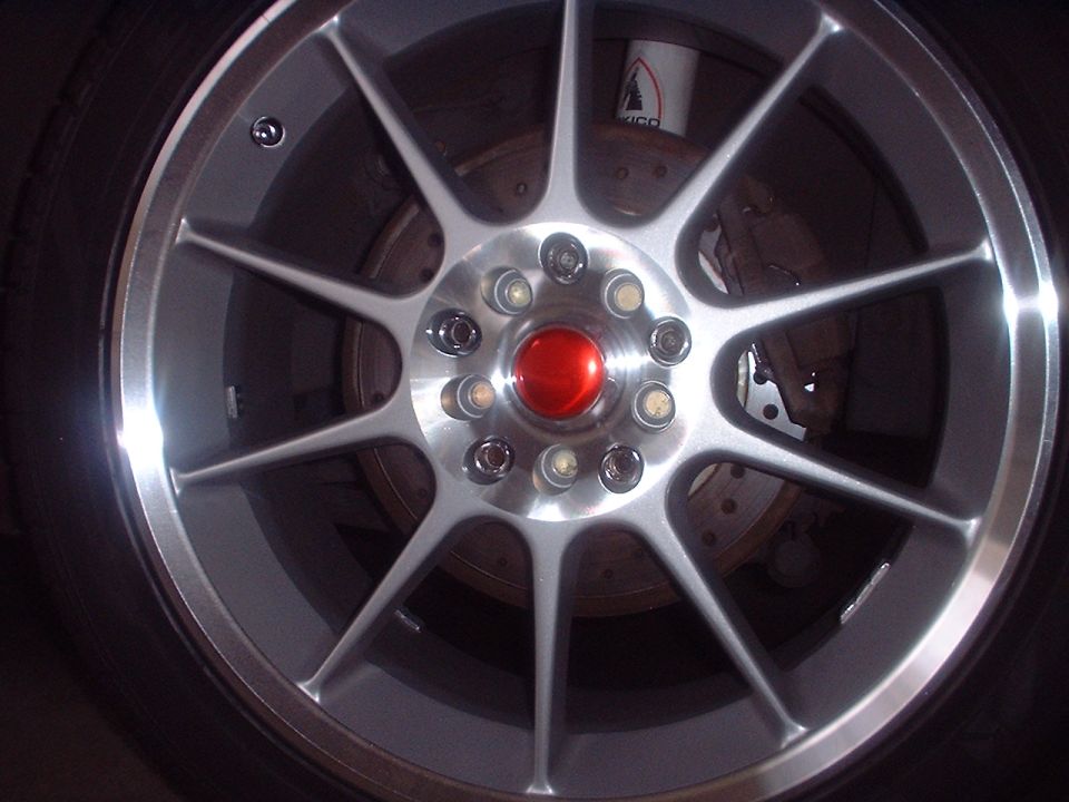 Close-up of silver multi-spoke alloy wheel with red center cap, brake rotor and caliper visible behind