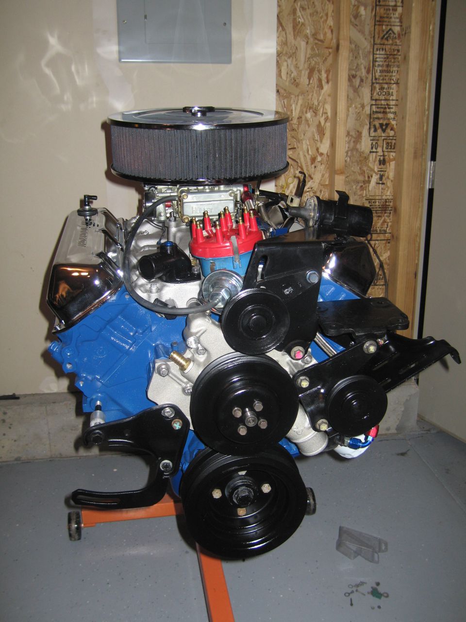 Blue Ford V8 engine with chrome valve covers and air cleaner on an orange engine stand in a garage