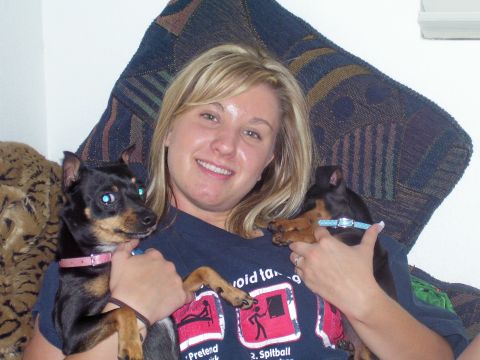 1991 Ford Bronco - A smiling person in a navy graphic T-shirt reclines against a patterned pillow holding two black-and-tan miniature pinscher dogs, one in a…